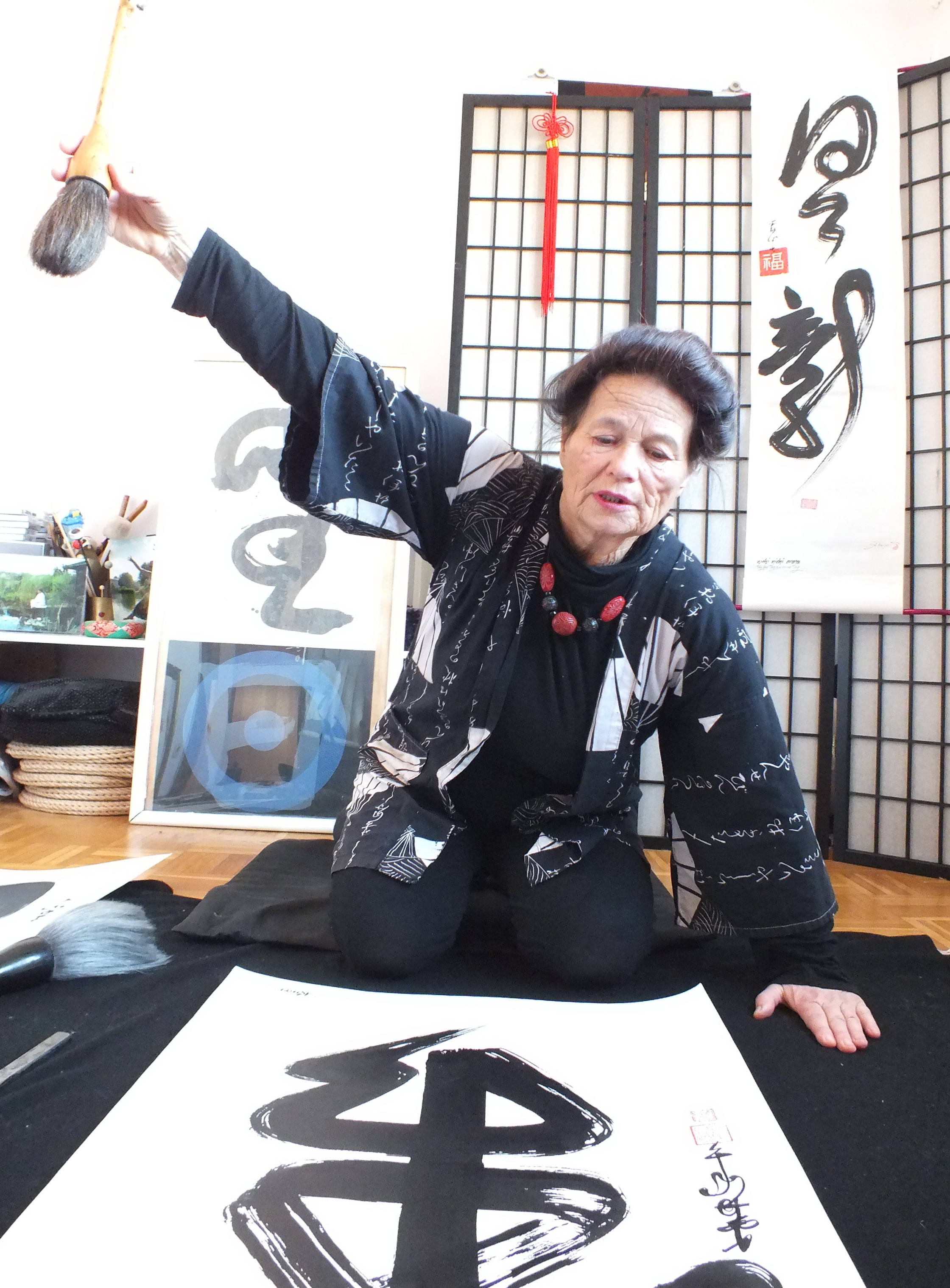 Eine Frau malt mit einem dicken Pinsel asiatische Schriftzeichen